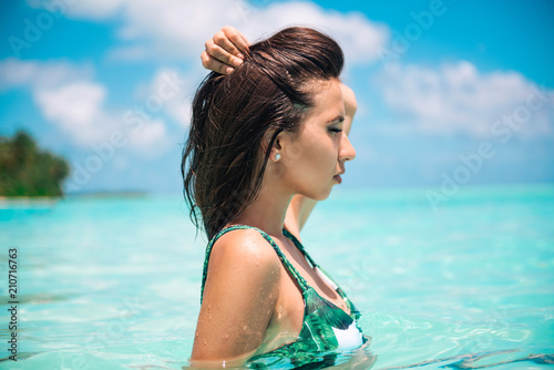 Beautiful young woman posing in sensual swimsuit sitting on a flamingo. Summer beach photo at Maldives. Water play.