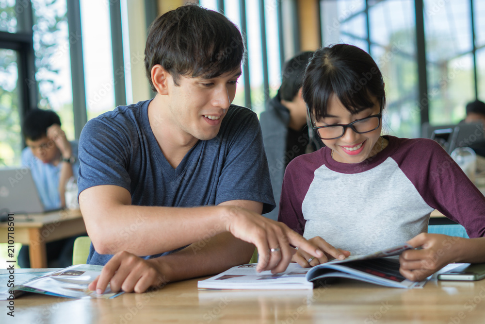 Reading a book together. Cheerful young man and woman reading book together while standing clode to each other in the library Reading a book together. Cheerful young man and woman reading book together while standing clode to each other in the library