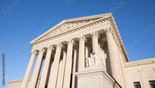 Looking up at the US Supreme Court building in Washington, DC with a bright blue sky.