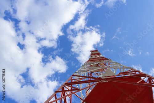 A red white telecommunications tower with a blue sky and white clouds.