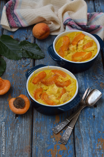 Clafouti with apricots in rameken on blue wooden background. Fruits clafoutis. Sweet casserole. Traditional French cake. Copy space.