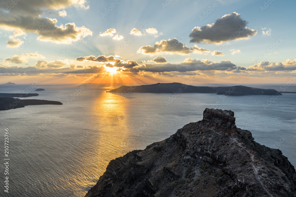 A view from the crater rim of an archipelago formed by a large volcanic crater, sunset with rays and smaller clouds - Location: Greece, Cyclades, Santorini (Santorin, Thira)