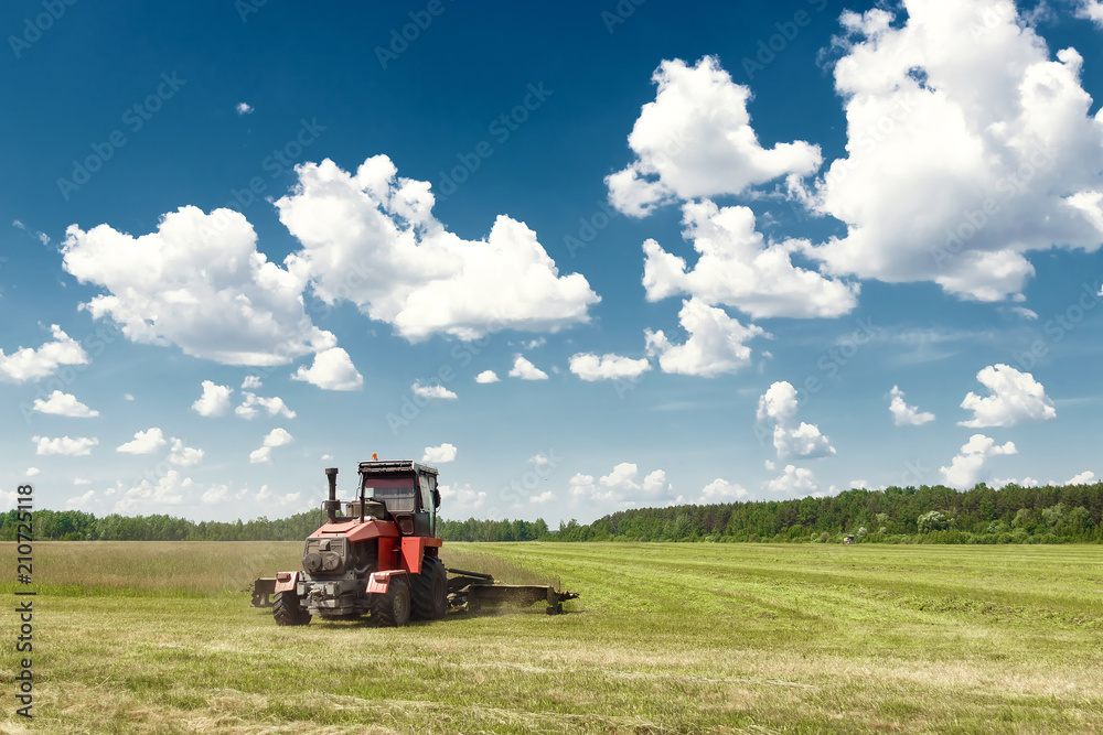 Agricultural machinery, harvester mowing grass in a field against a blue sky. Hay harvesting, grass harvesting. Season harvesting, grass, agricultural land. Agricultural machinery, harvester mowing grass in a field against a blue sky. Hay harvesting, grass harvesting. Season harvesting, grass, agricultural land.