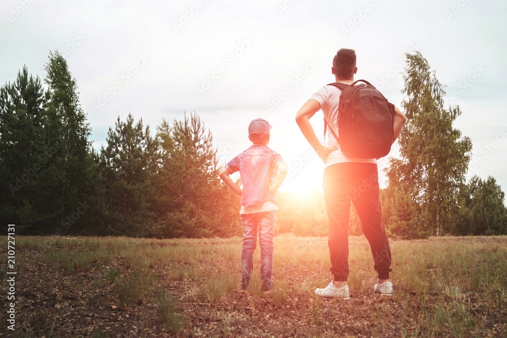 Fototapeta premium A man with a backpack, a father and his son on a hike, walking during walks in the woods. Family life, pastime with the family, the upbringing of children.