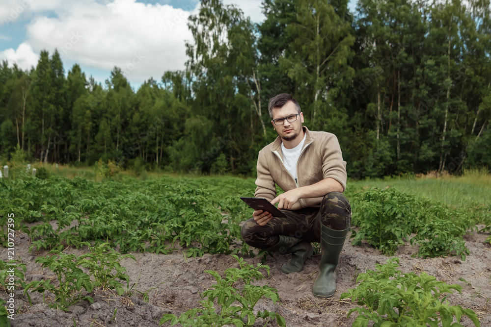 A male farmer sitting in the field and using a tablet. Modern application of technologies in agricultural activities. Farmland, new technologies, harvesting, fertilization, crop inspection. A male farmer sitting in the field and using a tablet. Modern application of technologies in agricultural activities. Farmland, new technologies, harvesting, fertilization, crop inspection.