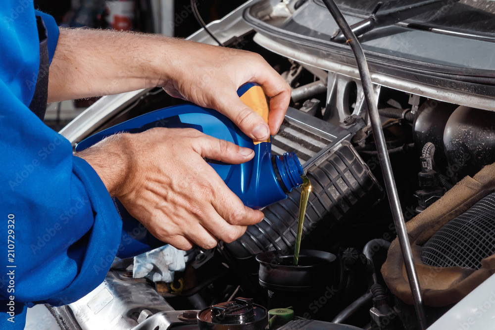 Obraz premium Male hands close-up pour oil into the motor. The auto mechanic works in the garage. Repair service. Maintenance of the car, car repair.