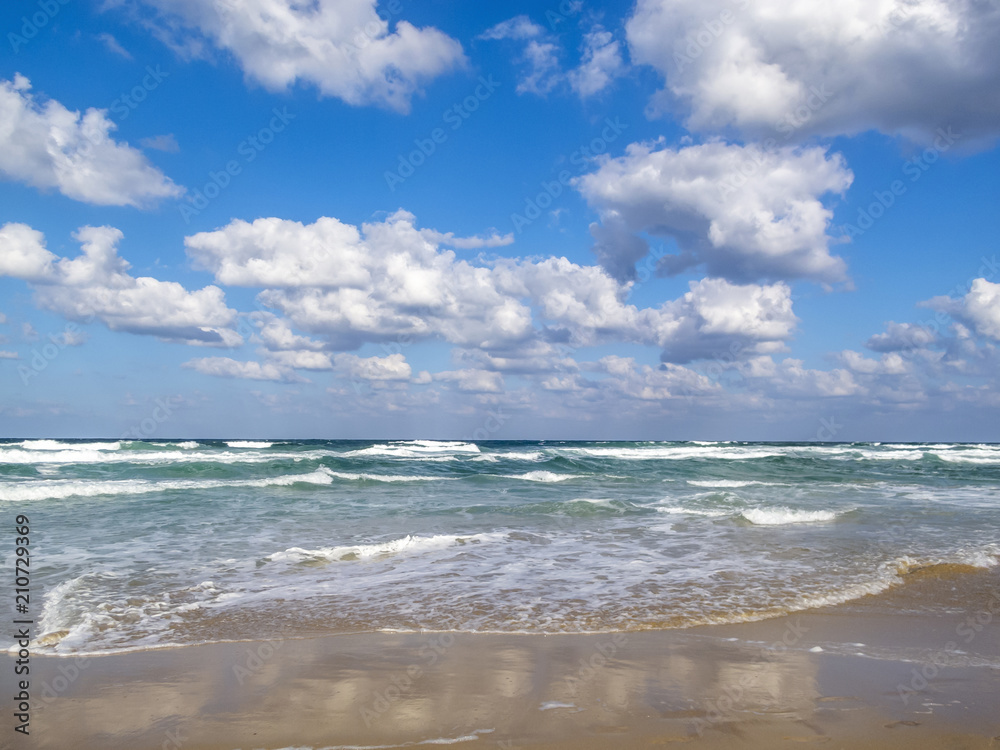 Waves spread on a sandy Black Sea beach, cloud reflections on the sand, cumulus clouds in the sky