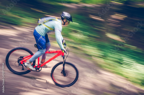 A cyclist in a helmet descends from the mountain on an orange bicycle, motion blur