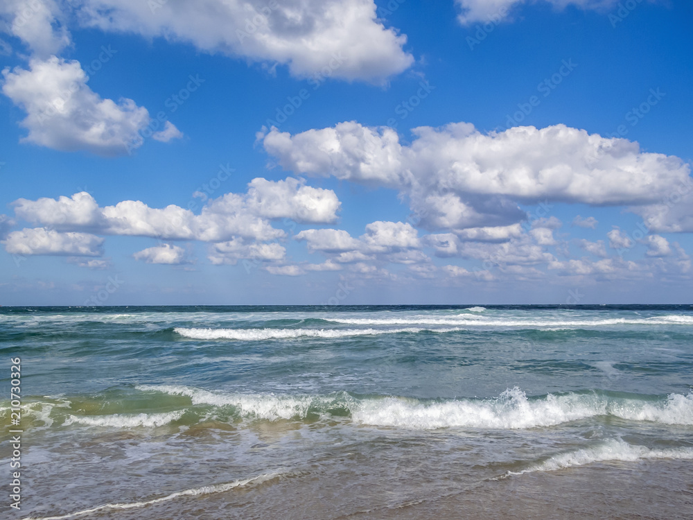 Waves spreading on a sandy Black Sea beach, cumulus clouds in the sky
