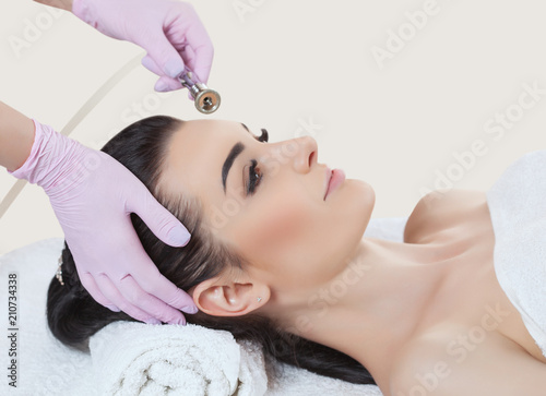 The cosmetologist makes the procedure Microdermabrasion of the facial skin of a beautiful, young woman in a beauty salon.Cosmetology and professional skin care. photo