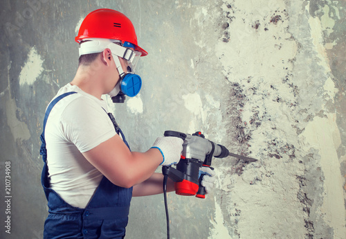 The builder with hammer drill perforator equipment making hole in wall at construction site. photo