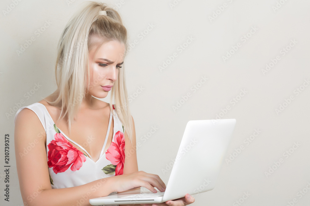 Serious pretty blonde girl lworking with the notebook, posing on the grey background, space for text Serious pretty blonde girl lworking with the notebook, posing on the grey background, space for text