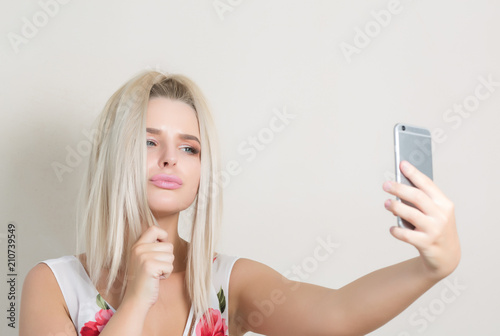 Cute blonde girl making self portrait on smartphone against a grey background