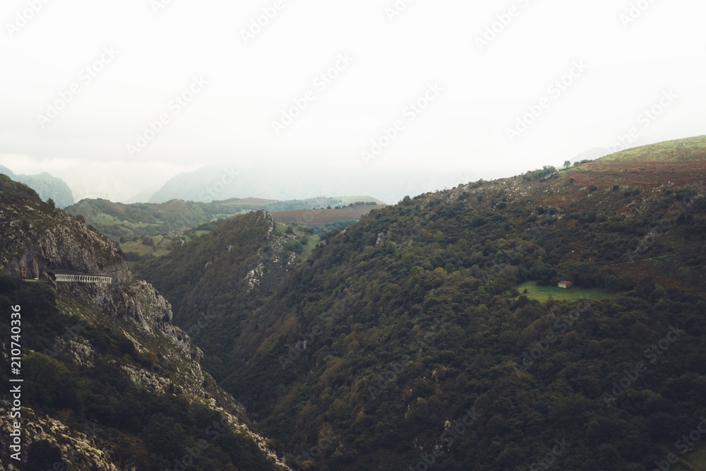 Obraz premium morning mist house in the mountain peaks on natural landscape. Green valley on background foggy dramatic sky, mountain tops. Panorama horizon perspective view of scenery hills. Travel mockup concept