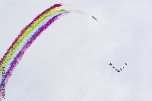 Fototapeta Naklejka Na Ścianę i Meble -  Airplanes on airshow with colorful multicolored trails of smoke against a blue sky. Aircraft, flying display and aerobatic show