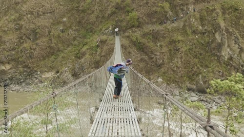 Local men carries a heavy load on suspension bridge over the river in Nepal. photo