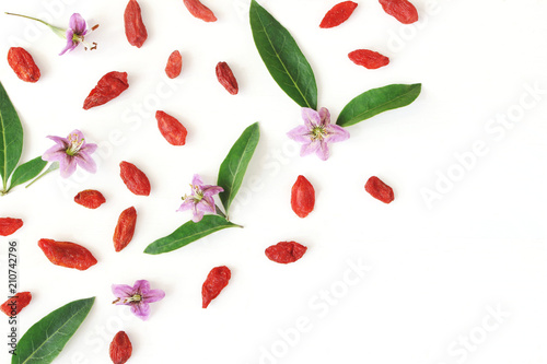 Closeup of Goji berries, Lycium barbarum. Dried Asian fruit, leaves and blossoms isolated on white wooden background. Healthy superfood. Floral pattern, decorative corner. Flatlay, top view.