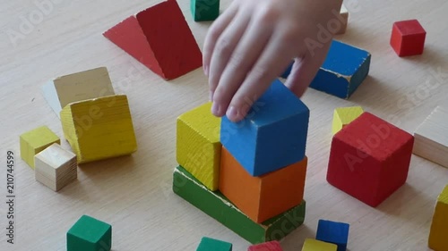 Caucasian kid playing with wooden bricks. Children constructing house from colored elements. Bright toy building - real estate theme. Closeup view.