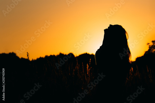 Silhouette of a girl who laughs in among the high grass on the background of the evening sky