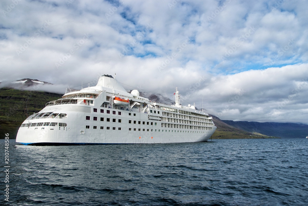 Ocean liner in sea on mountain landscape in Sejdisfjordur, Iceland. Cruise ship in sea with mountains on cloudy sky. Cruising for pleasure. Summer vacation and trip. Adventure and discovery