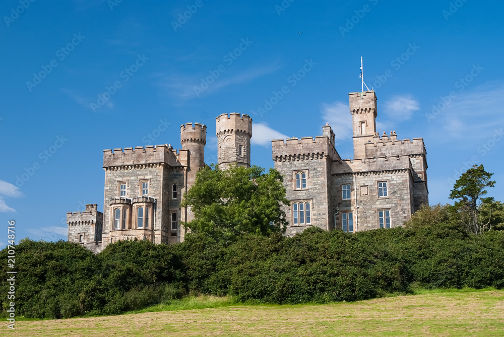 Lews Castle on blue sky in Stornoway, United Kingdom. Castle with green trees on natural landscape. Victorian style architecture and design. Landmark and attraction. Summer vacation and wanderlust