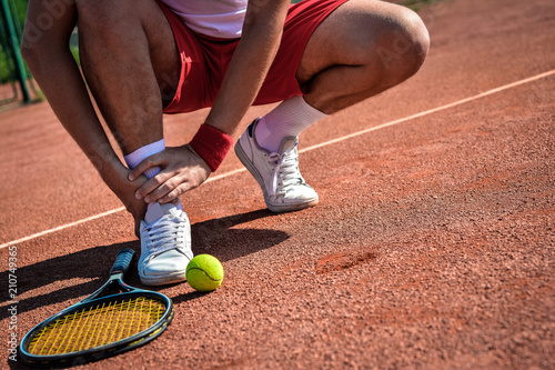 Sports injury. Close-up of tennis player touching his leg while sitting on the tennis court