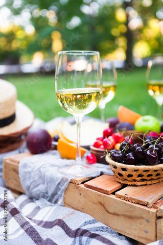 Picnic background with white wine and summer fruits on green grass, summertime party