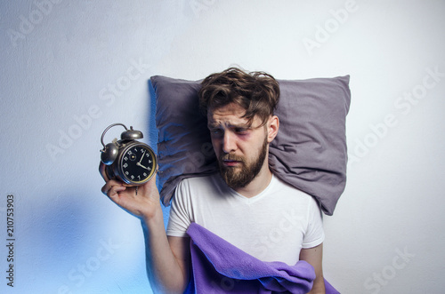 Foto Man laying sad and awake in bed, while looking to alarm clock, sleep disorder