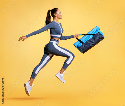 Go to training. Sporty woman with bag running in silhouette on yellow background. Dynamic movement. Side view. Sports and healthy lifestyle