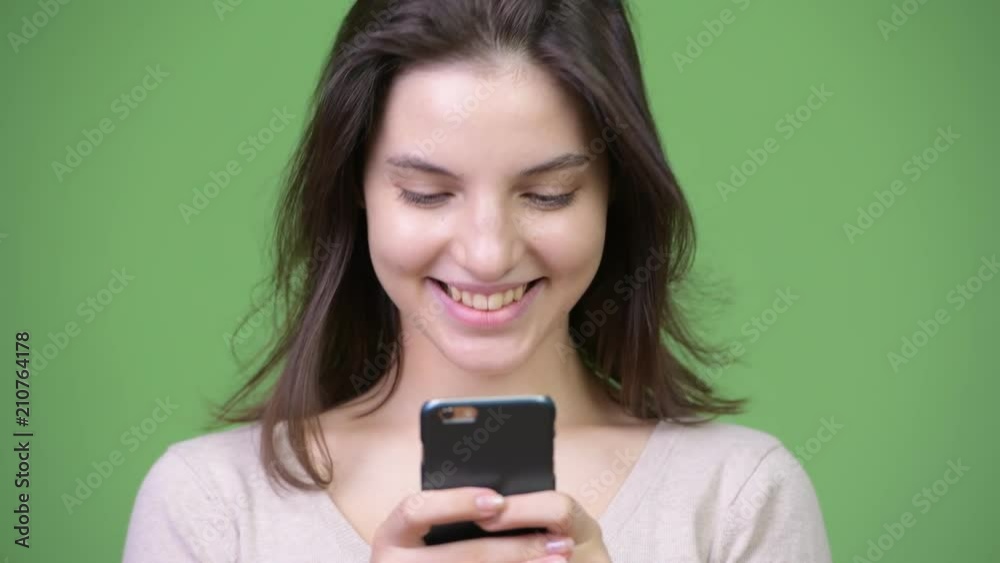 Young happy beautiful woman smiling while using phone against green background Young happy beautiful woman smiling while using phone against green background