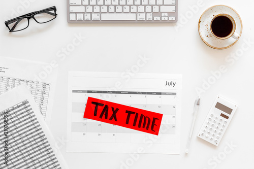 Tax time lettering on office work desk with calendar and bills on white background top view copy space