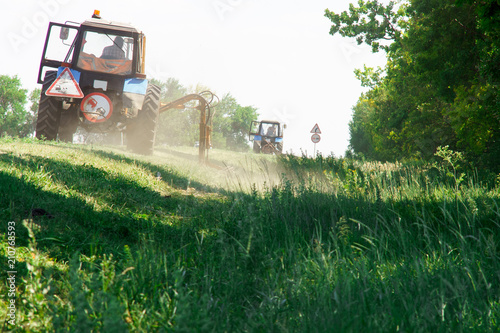 Tractors machines mowing lawn grass along road