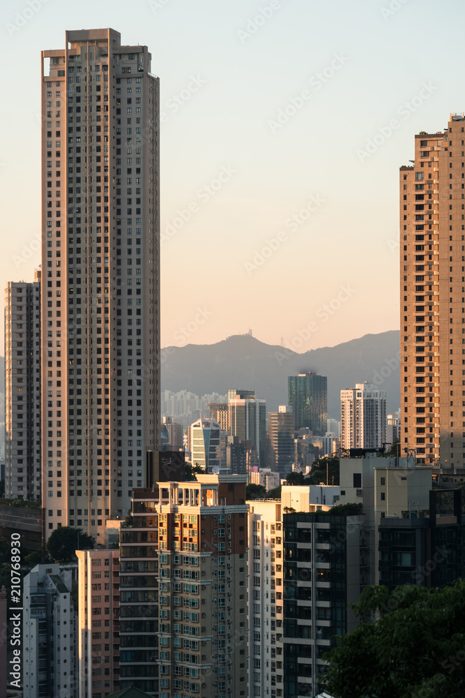 Fototapeta premium Sunset over tall apartment tower in Happy Valley in Hong Kong island with the peaks of kowloon in the back in Hong Kong, China