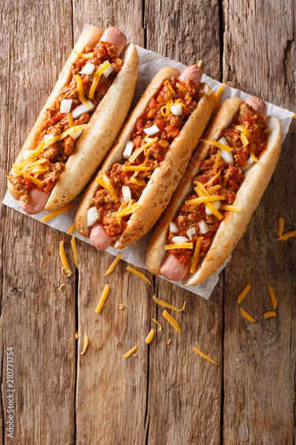 Traditional American chili hot dogs with cheddar cheese, onion and spicy sauce closeup. vertical top view