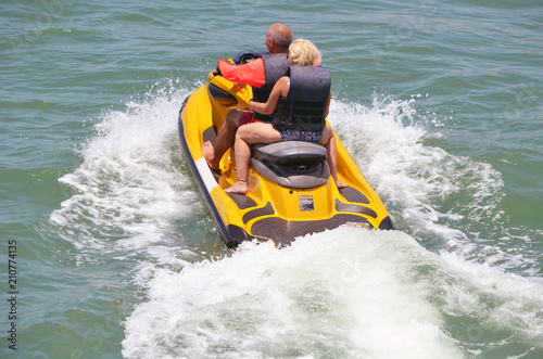 An older senior couple riding tandem on a bright yellow jet ski on the Florida Intra-coastal Waterway near Miami Beach.