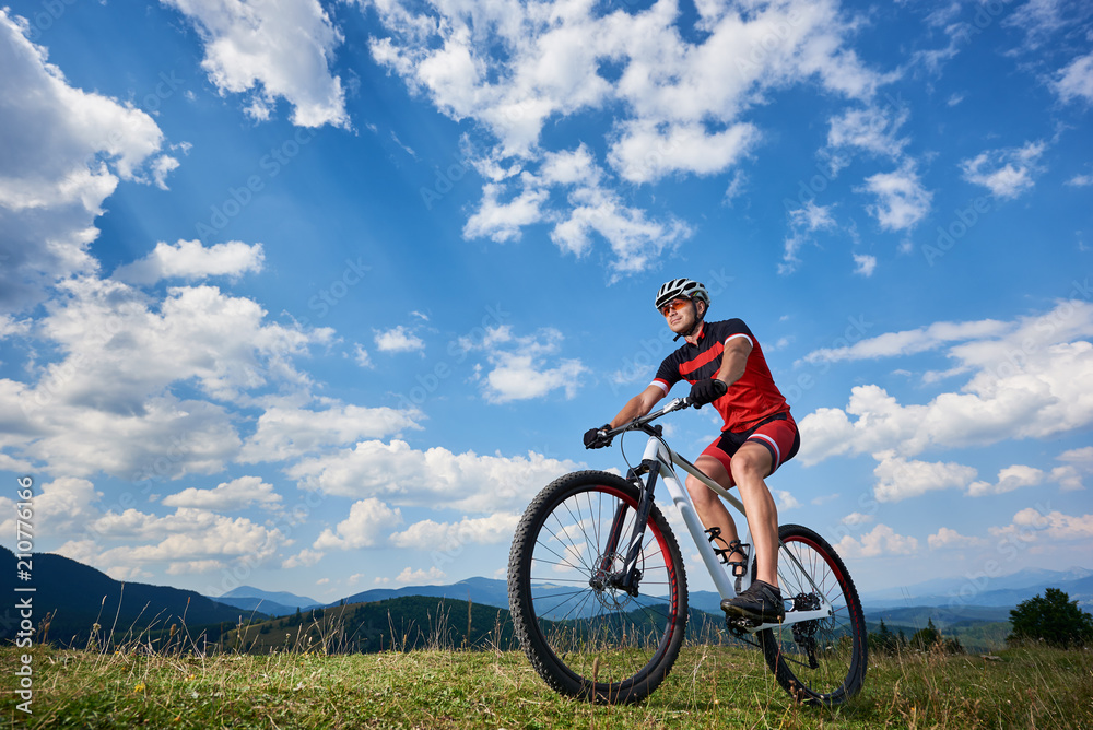 Athletic professional sportsman cyclist in sportswear and helmet cycling cross country bike in Carpathian mountains against blue sky with clouds on summer. Active lifestyle and outdoor sport concept