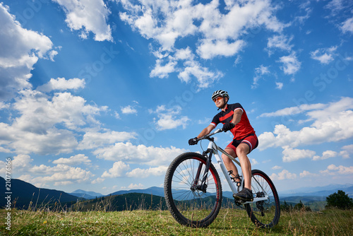 Athletic professional sportsman cyclist in sportswear and helmet cycling cross country bike in Carpathian mountains against blue sky with clouds on summer. Active lifestyle and outdoor sport concept