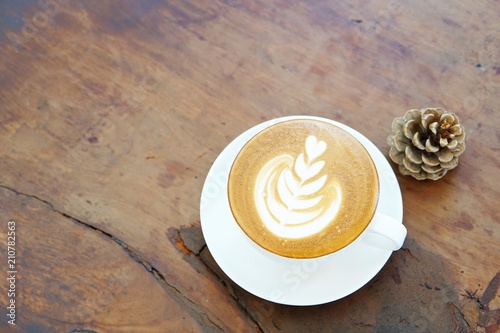 A white cup of coffee with latte art, pine cone on wooden table, top view, copy space