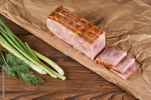 ham on kraft paper with green onion and parsley on a wooden background photo