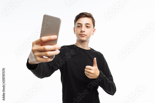 Portrait of an emotional teenager who takes a selfie on a smartphone, in a black t-shirt, on a white background, advertising, text insertion