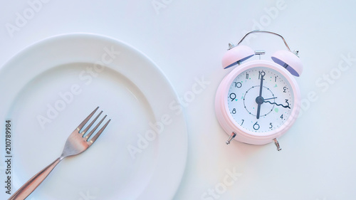 clock on an empty plate, white background. the concept of limiting the intake of food.