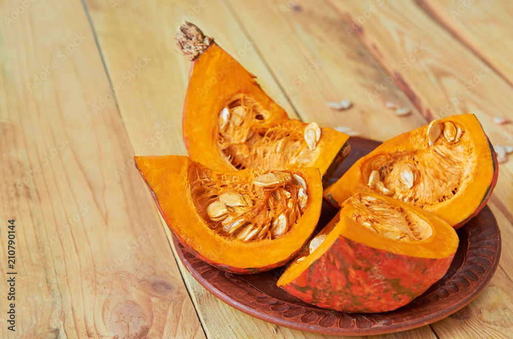 Pumpkin slices with seeds on the brown plate on the wooden background. Ingredients for tasty diet autumn dish. Side view