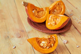 Pumpkin slice with fresh seeds on the wooden kitchen table. Three pieces of sliced pumpkin on the brown plate on the blurred background. Ingredients for diet autumn dish. Close up view