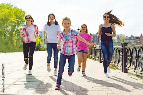 Group of mothers and daughters are running along the road in the park. Urban background