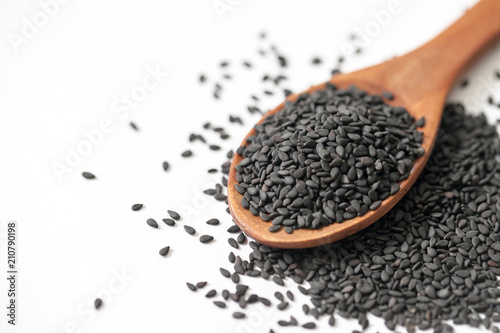 black sesame seeds in wooden spoon on white background