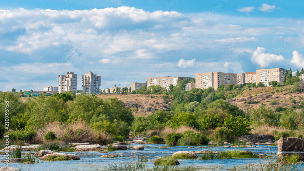 Fototapeta premium Yuzhnoukrainsk on the rocky bank of the river. Summer landscape with river flow and with stones and green vegetation.