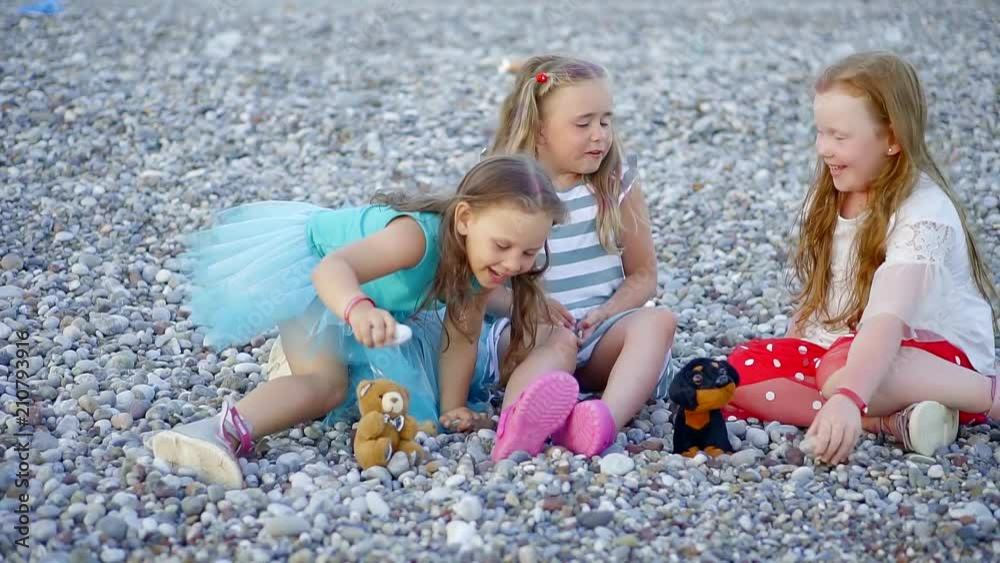 Three happy children talking and playing on the pebble beach. Three happy children talking and playing on the pebble beach.