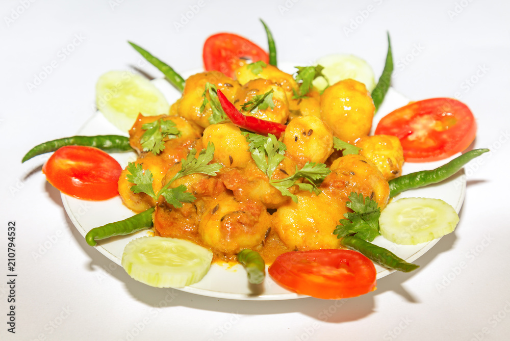 Indian vegetarian food dish prepared with small potatoes popularly known as Dum Alu garnished with cucumber, tomato and green chilli.
