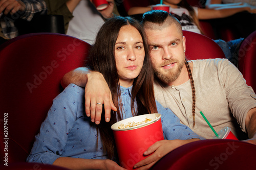 friends sitting in cinema watch film eating popcorn and drinking water.