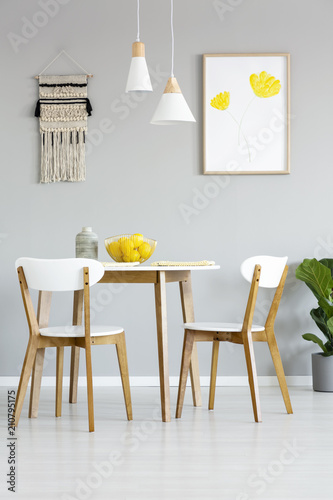 Real photo of a simple  natural dining room interior with lamps and poster with yellow flowers above a round  wooden table with matching chairs